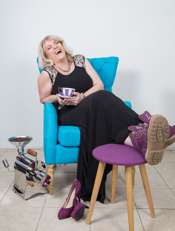 Image of Tamara Reeves sitting down on a blue chair holding a cup of coffee and laughing.